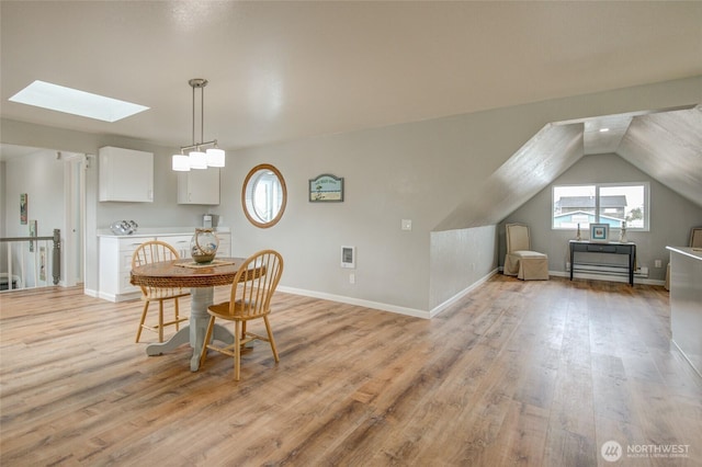 dining room featuring a skylight, light wood-style floors, baseboards, and vaulted ceiling