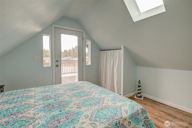 bedroom featuring wood finished floors, a skylight, vaulted ceiling, baseboards, and access to exterior