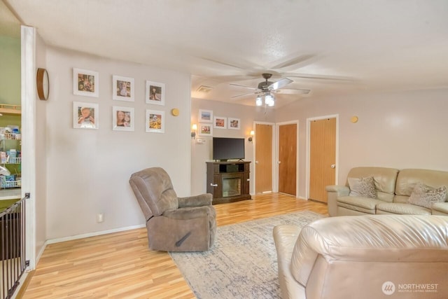 living area with light wood finished floors, ceiling fan, baseboards, and a fireplace