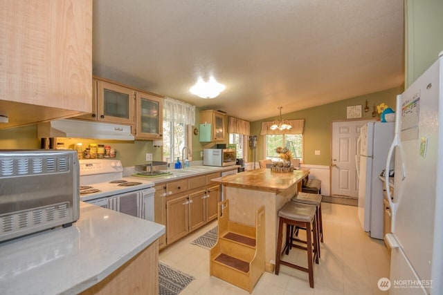 kitchen with under cabinet range hood, white appliances, a kitchen island, a sink, and a chandelier