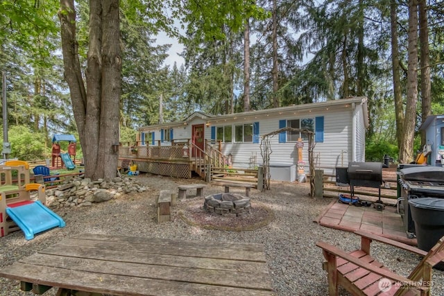 back of house featuring an outdoor fire pit, a deck, and a playground