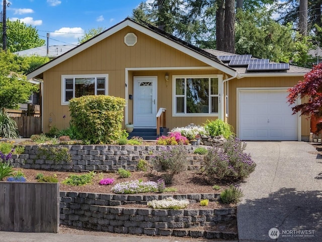view of front of home with an attached garage, roof mounted solar panels, concrete driveway, fence, and entry steps