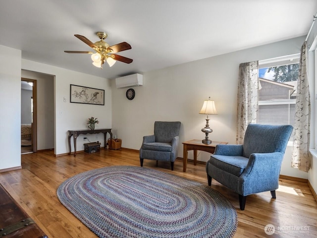 sitting room featuring a wall mounted air conditioner, ceiling fan, wood finished floors, and baseboards