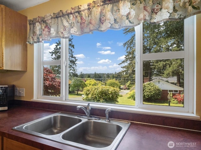 kitchen featuring a sink, healthy amount of natural light, brown cabinets, and dark countertops