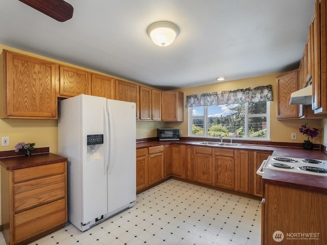 kitchen featuring white refrigerator with ice dispenser, a sink, and dark countertops