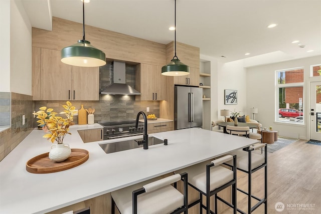 kitchen with high end appliances, wall chimney range hood, modern cabinets, a sink, and a kitchen breakfast bar