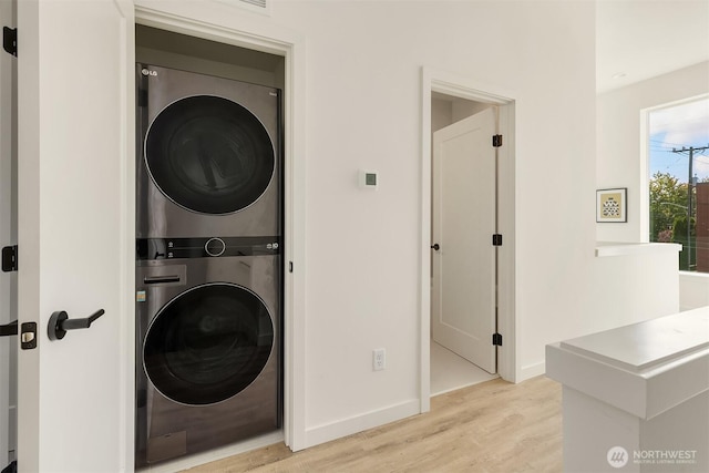 laundry room with stacked washer / dryer, light wood-type flooring, and baseboards