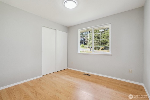 unfurnished bedroom featuring light wood-type flooring, baseboards, and a closet
