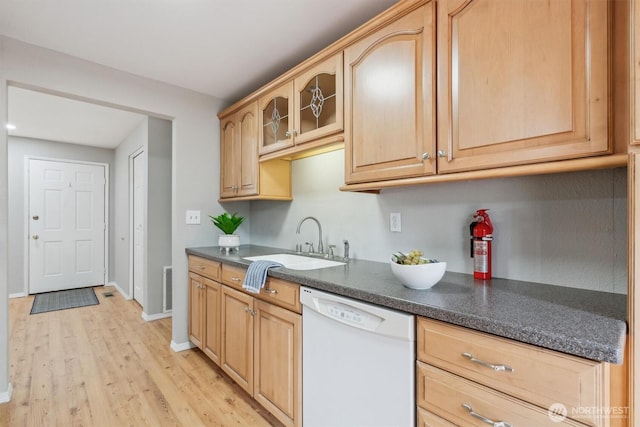 kitchen featuring white dishwasher, a sink, dark countertops, light wood finished floors, and glass insert cabinets