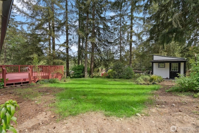 view of green lawn with a wooden deck, view of scattered trees, and an outbuilding