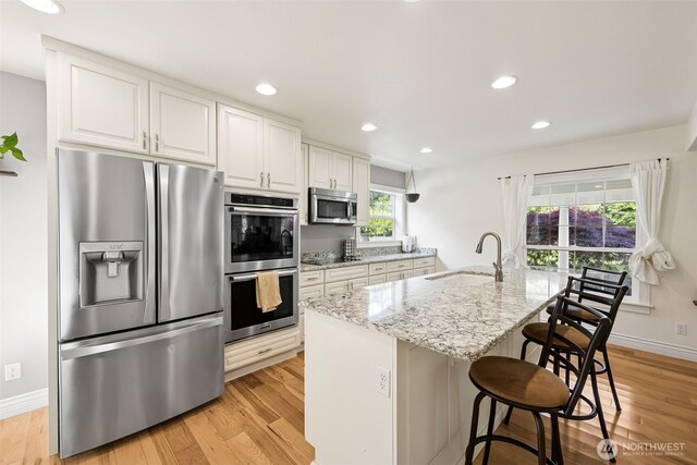 kitchen with appliances with stainless steel finishes, a sink, light stone counters, light wood-type flooring, and recessed lighting