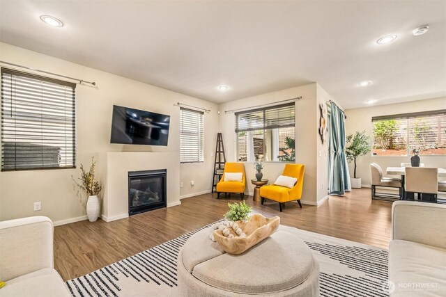 living room with wood finished floors, a glass covered fireplace, recessed lighting, and baseboards