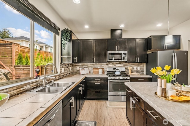kitchen with appliances with stainless steel finishes, a sink, light wood-type flooring, decorative backsplash, and recessed lighting