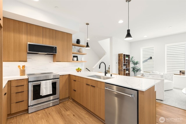 kitchen with stainless steel appliances, a sink, a peninsula, light wood-style flooring, and modern cabinets