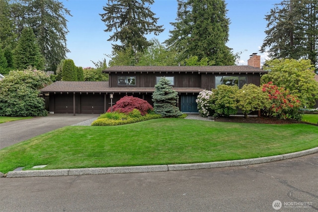 view of front of home with a chimney, an attached garage, a front yard, and driveway