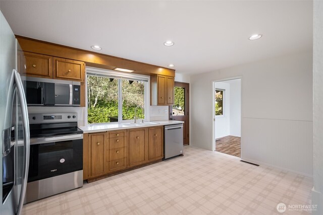 kitchen with appliances with stainless steel finishes, a sink, brown cabinetry, light countertops, and light flooring