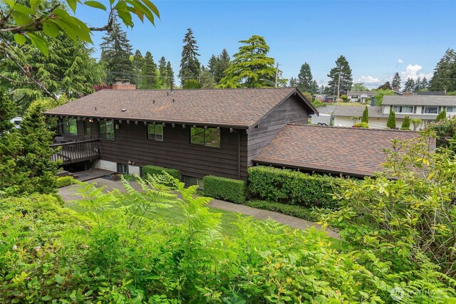 view of side of property featuring a wooden deck, a chimney, and roof with shingles