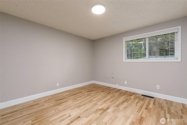empty room with light wood finished floors, baseboards, and a textured ceiling