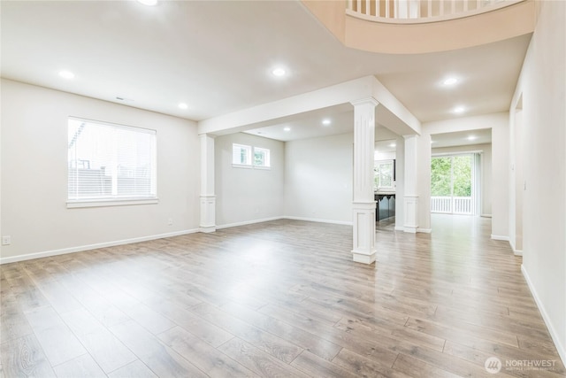 unfurnished living room with ornate columns, light wood finished floors, baseboards, and recessed lighting