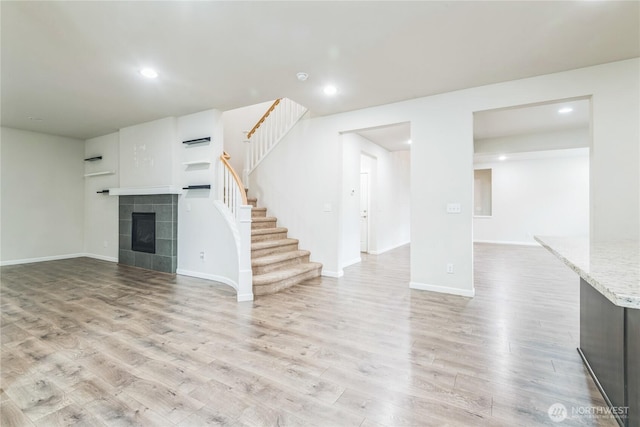 unfurnished living room with light wood finished floors, a tile fireplace, stairway, recessed lighting, and baseboards