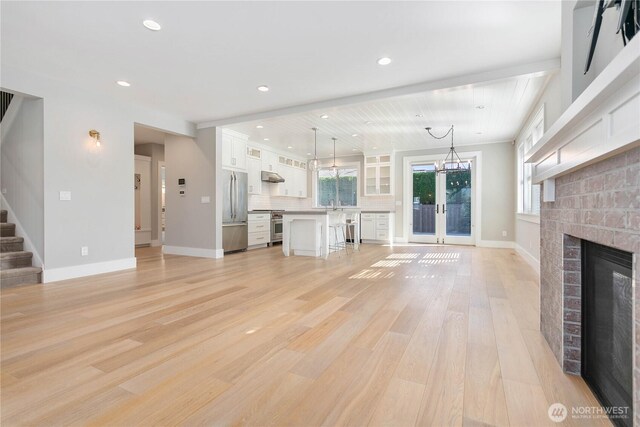 unfurnished living room with light wood-style floors, stairs, recessed lighting, a brick fireplace, and french doors