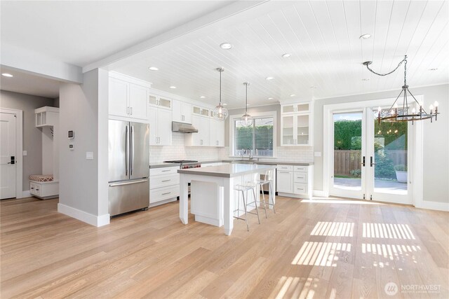 kitchen featuring stainless steel appliances, a breakfast bar, under cabinet range hood, light wood-type flooring, and tasteful backsplash