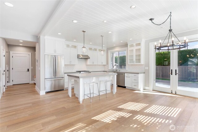 kitchen with stainless steel appliances, a breakfast bar area, light wood-style flooring, white cabinetry, and backsplash