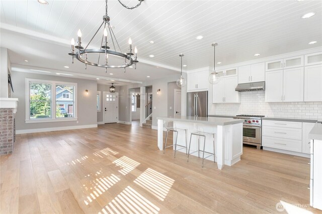 kitchen with appliances with stainless steel finishes, under cabinet range hood, a chandelier, a center island, and white cabinetry