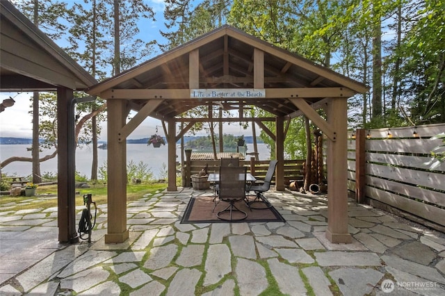 view of patio / terrace featuring a gazebo, fence, outdoor dining area, and a water view