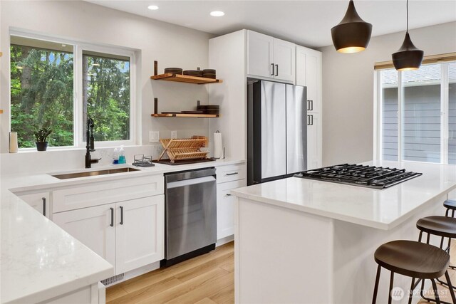 kitchen featuring stainless steel appliances, open shelves, a sink, a breakfast bar, and light wood-type flooring