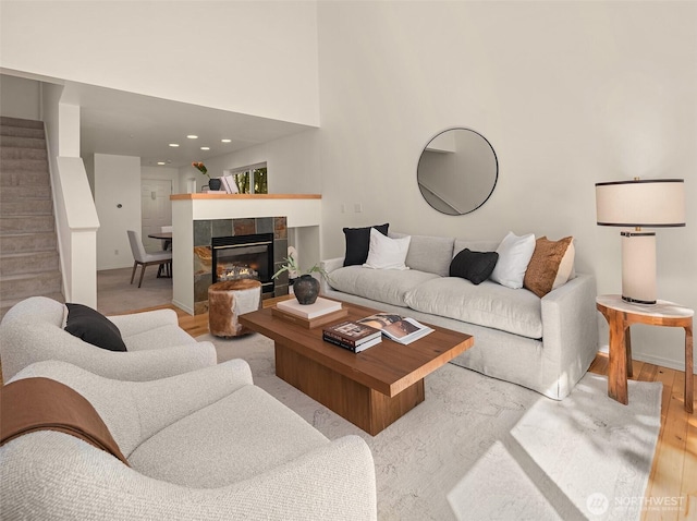 living room with stairs, light wood-style floors, baseboards, and a tile fireplace