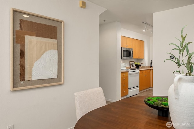 kitchen featuring white electric range oven, stainless steel microwave, baseboards, light wood-style flooring, and rail lighting