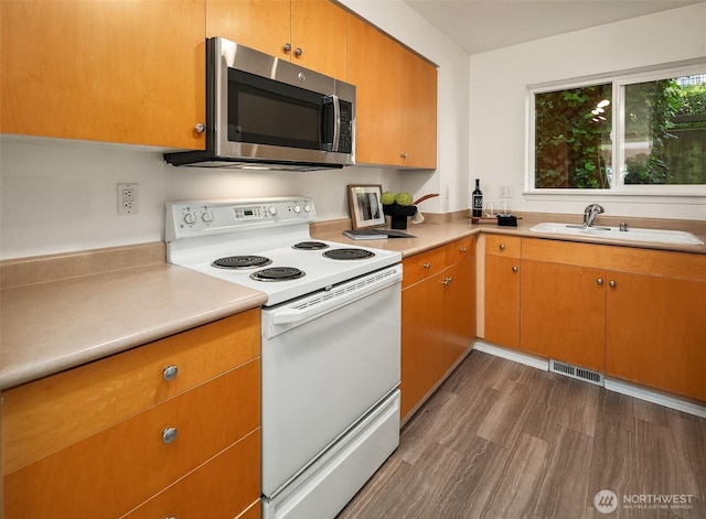 kitchen with stainless steel microwave, white range with electric stovetop, a sink, light countertops, and dark wood-style floors