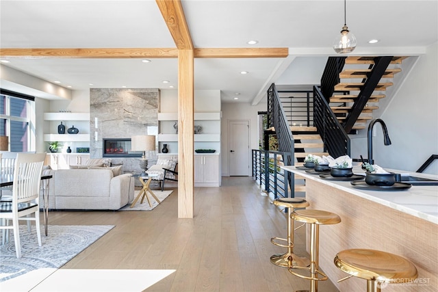 living area featuring stairs, healthy amount of natural light, light wood-type flooring, beamed ceiling, and recessed lighting
