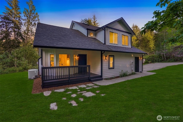 back of property at dusk featuring a yard, covered porch, and roof with shingles