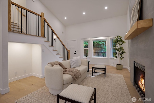 living room with light wood-type flooring, recessed lighting, a large fireplace, stairs, and baseboards
