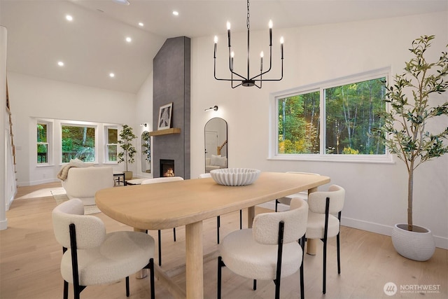 dining area featuring high vaulted ceiling, baseboards, a large fireplace, light wood-type flooring, and healthy amount of natural light
