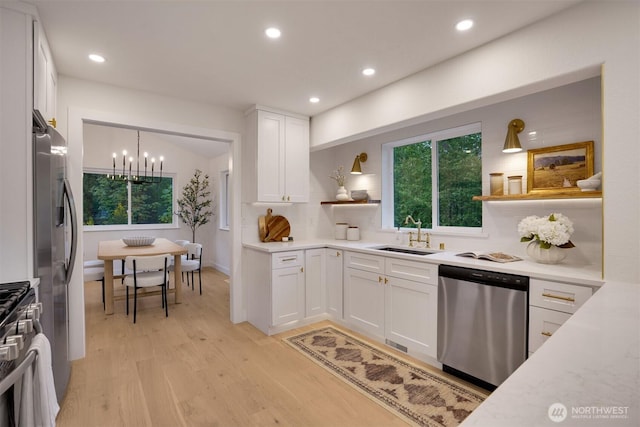 kitchen featuring appliances with stainless steel finishes, a sink, open shelves, light wood-style floors, and white cabinets