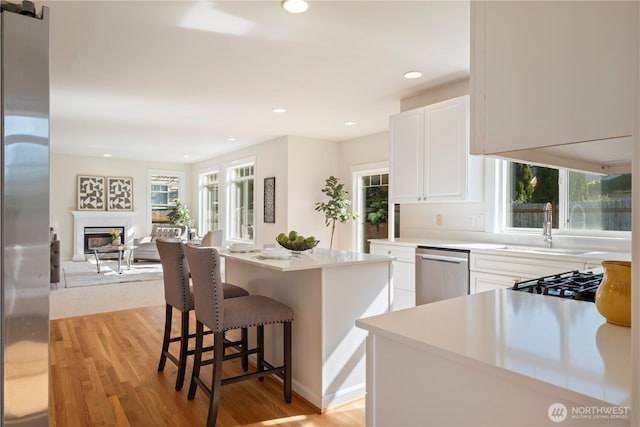 15704 124th Ave NE, Woodinville, WA 98072 - kitchen featuring stainless steel dishwasher, white cabinets, a glass covered fireplace, light wood-style floors, and a sink