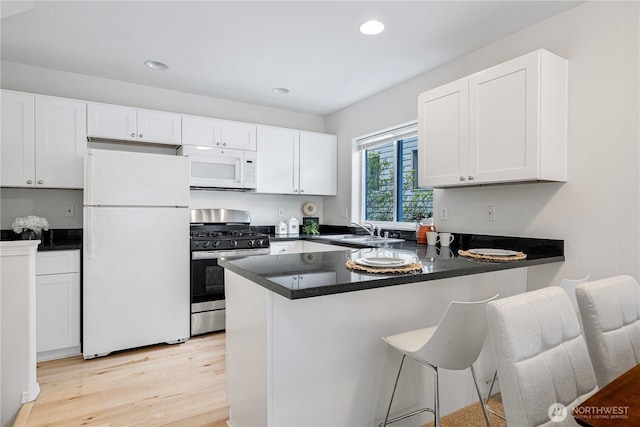 kitchen featuring white appliances, light wood-style flooring, white cabinets, a peninsula, and a sink