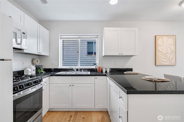 kitchen with white appliances, a sink, white cabinetry, light wood finished floors, and a peninsula