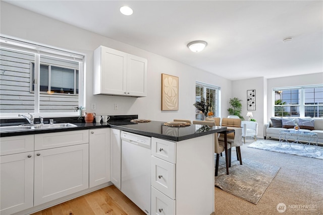 kitchen featuring a sink, dishwasher, a peninsula, open floor plan, and white cabinets