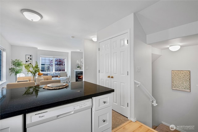 kitchen with dishwasher, white cabinetry, a warm lit fireplace, and dark countertops
