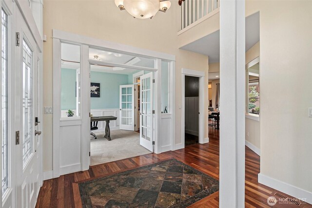 foyer entrance featuring wood finished floors, a towering ceiling, wainscoting, french doors, and a decorative wall
