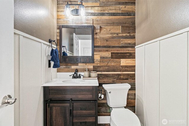 bathroom with toilet, wooden walls, vanity, and a textured wall