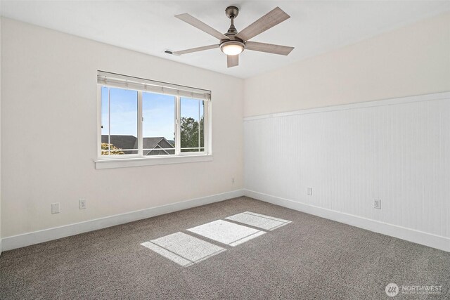 carpeted spare room with ceiling fan, baseboards, and a wainscoted wall