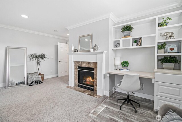 carpeted home office with ornamental molding, built in desk, a tiled fireplace, baseboards, and recessed lighting