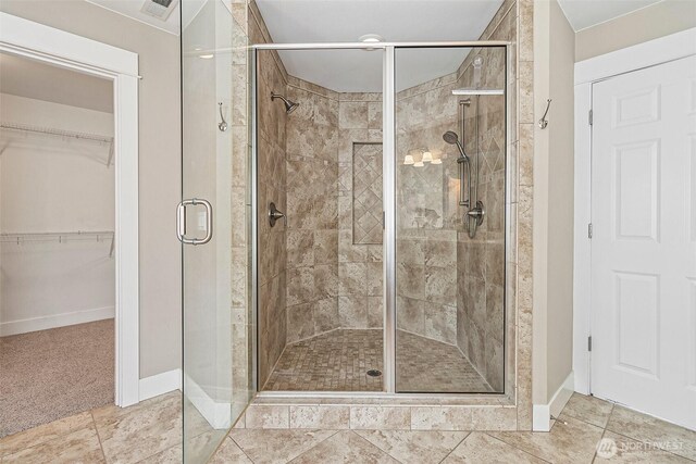 full bath with a shower stall, baseboards, a walk in closet, and tile patterned floors