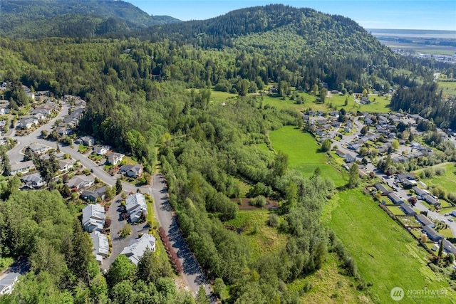 view of property location featuring a heavily wooded area, mountains, and nearby suburban area