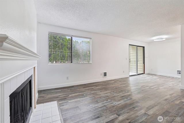 unfurnished living room with a textured ceiling, wood finished floors, a tiled fireplace, and baseboards
